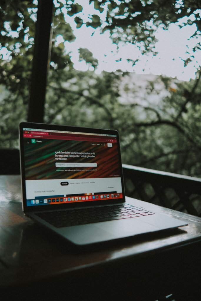 pexels-photo-18096282-18096282 Open laptop showing a website screen on a wooden table in an outdoor terrace setting.
