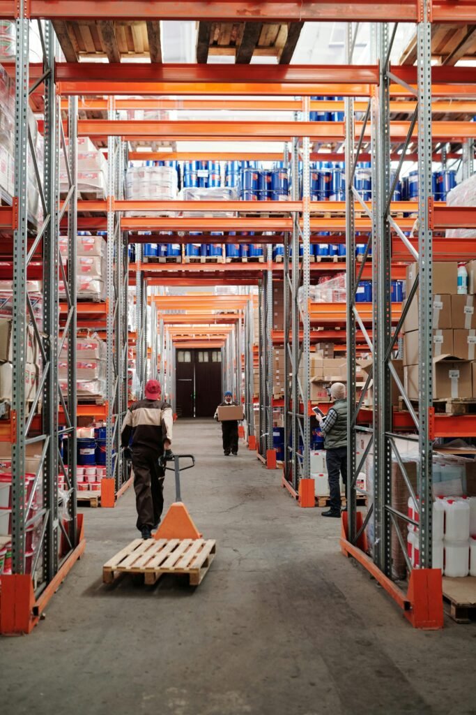 pexels-photo-4483772-4483772 Workers arrange inventory on shelves in a large industrial warehouse.