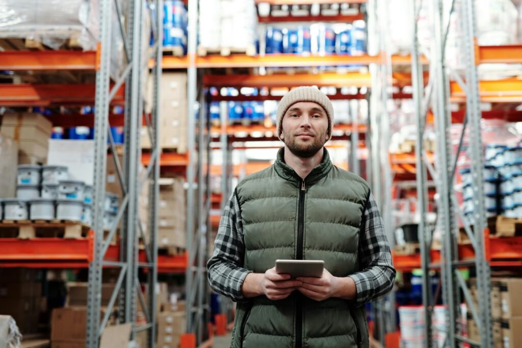 pexels-photo-4484078-4484078 A warehouse worker wearing a beanie uses a tablet to manage inventory in a storeroom with shelves.