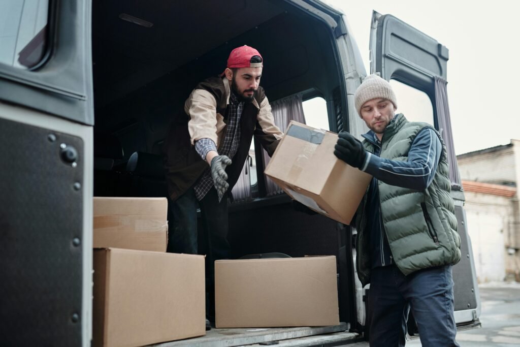 pexels-photo-4487512-4487512 Two delivery workers unload cardboard boxes from a van, showcasing teamwork and logistics.