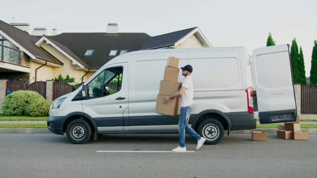 pexels-photo-5025669-5025669 Man unloading cardboard boxes from a delivery van in a suburban neighborhood street.
