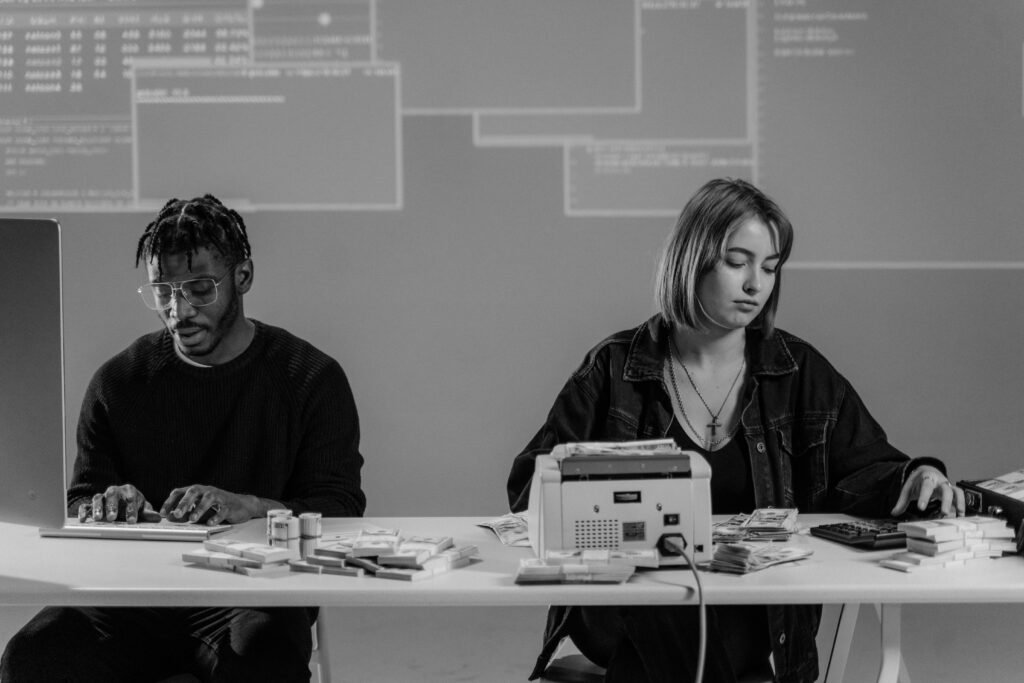 pexels-photo-6266275-6266275 Two professionals working with computers and currency at a desk in a modern office setting.