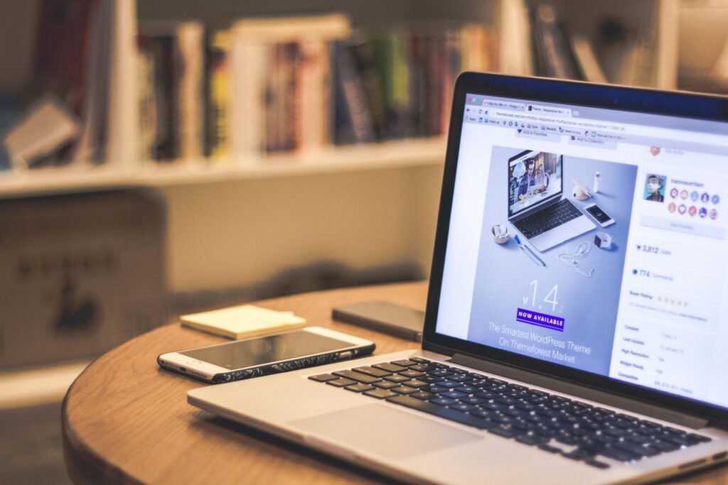 pexels-photo-69432-69432 A cozy modern workspace featuring a laptop displaying a website, a smartphone, and books on shelves.